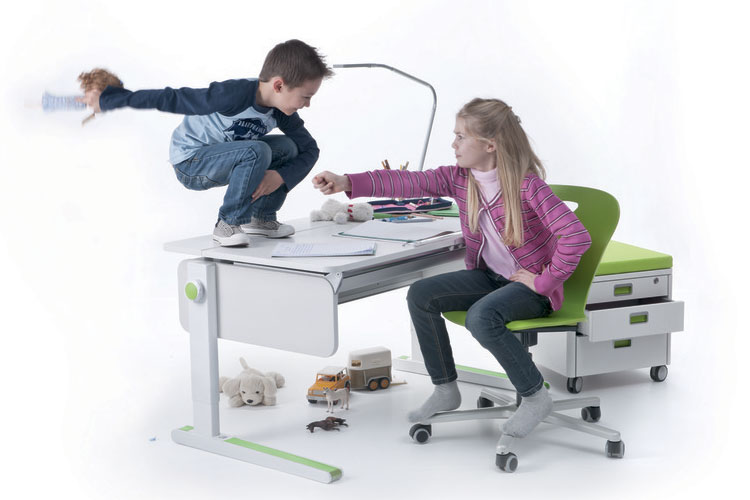 Junge hockt auf weißem Schreibtisch, Mädchen sitzt auf grünem Stuhl