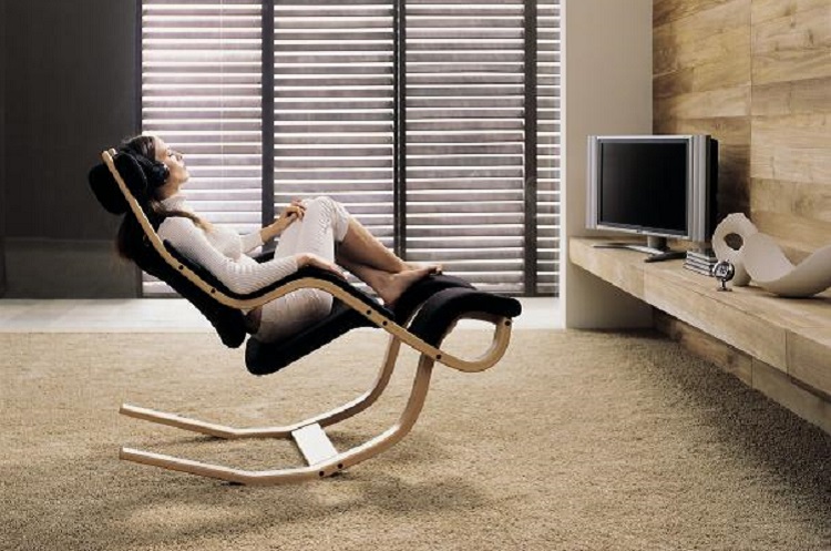 Frau entspannt mit Kopfhörern auf einem Schaukelstuhl aus Holz